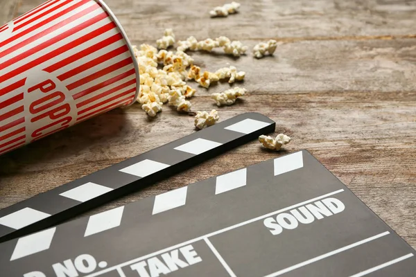 Film klepel en popcorn op houten achtergrond, close-up — Stockfoto