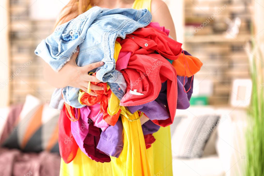 Woman holding pile of colorful clothes indoors