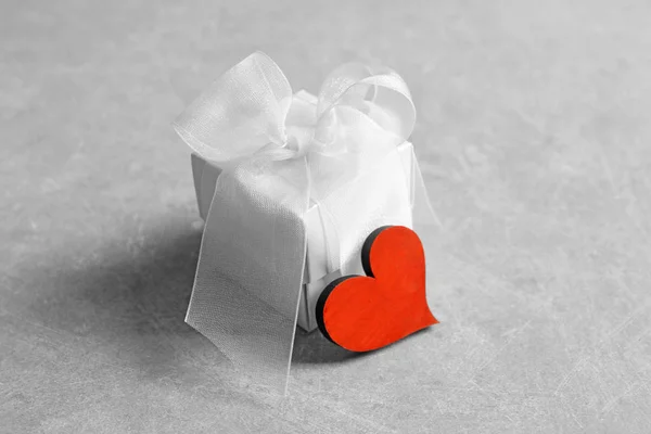 Gift box and small heart on grey background