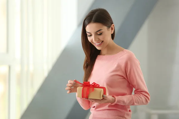 Beautiful young woman holding gift box at home — Stock Photo, Image