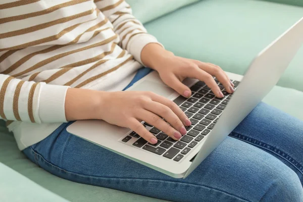 Young woman with modern laptop sitting on sofa at home, closeup