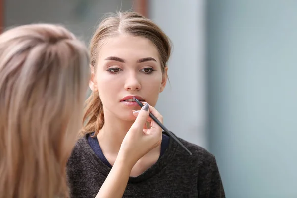 Artista profesional creando maquillaje para hermosa modelo sobre fondo borroso —  Fotos de Stock