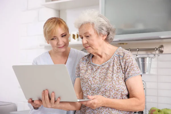 Mulher sênior e cuidador com laptop em casa — Fotografia de Stock