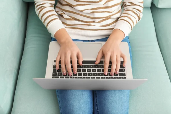 Young woman with modern laptop sitting on sofa at home