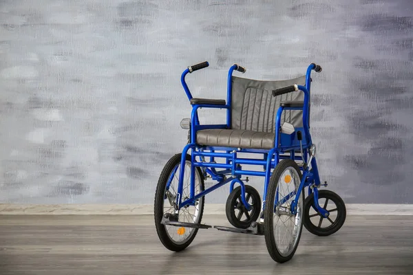 Cadeira de rodas azul perto da parede cinza dentro de casa — Fotografia de Stock