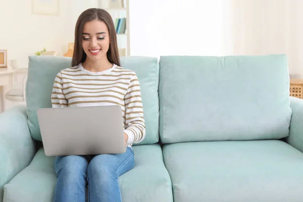 Jovem mulher com laptop moderno sentado no sofá em casa — Fotografia de Stock