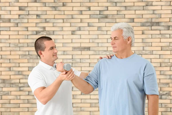 Physiotherapist working with patient on brick wall background — Stock Photo, Image