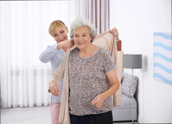 Opiekun, pomagając starszy kobieta umieścić na sweter w domu — Zdjęcie stockowe
