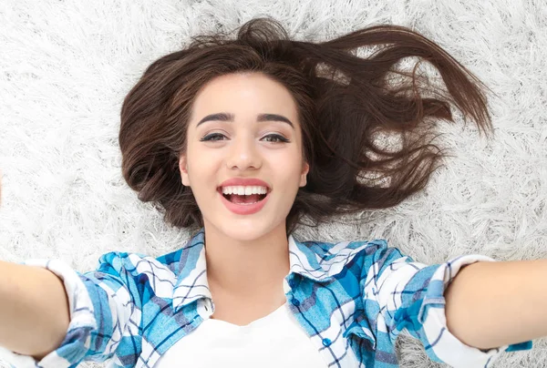 Vackra leende kvinna tar selfie liggande på matta hemma — Stockfoto