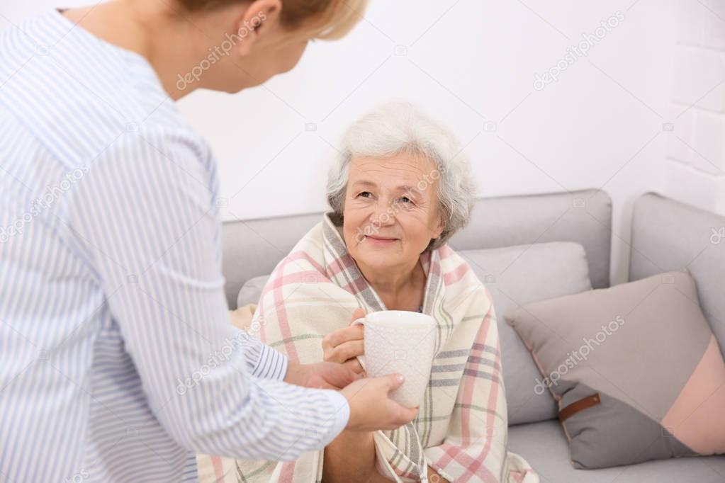 Caregiver giving cup of tea to senior woman at home