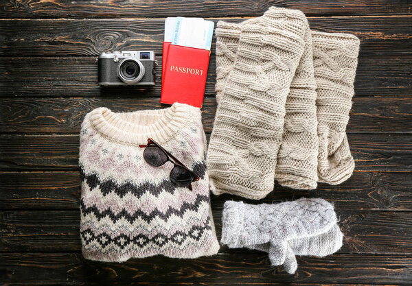 Warm clothes with photo camera and documents on wooden background. Winter vacation concept