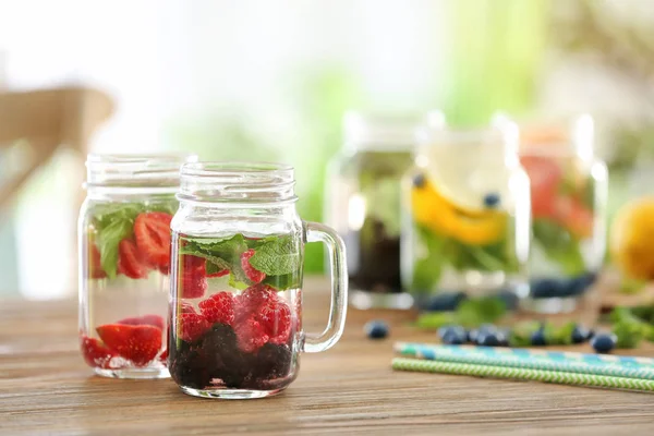 Mason jars of infused water with berries on wooden table