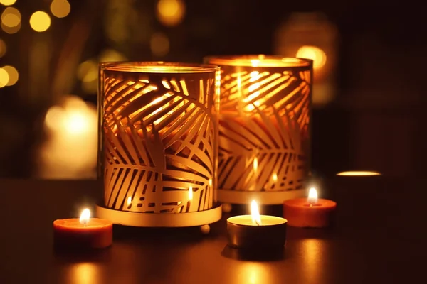 Beautiful holders with burning candles in darkness against defocused lights — Stock Photo, Image