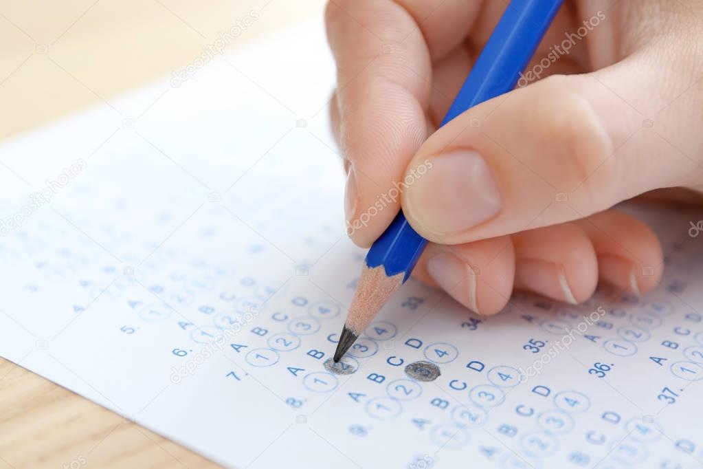 Student choosing answers in test form to pass exam at table