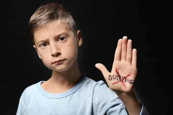 Niño con la palabra cruzada "Bullying" en su mano contra el fondo negro — Foto de Stock