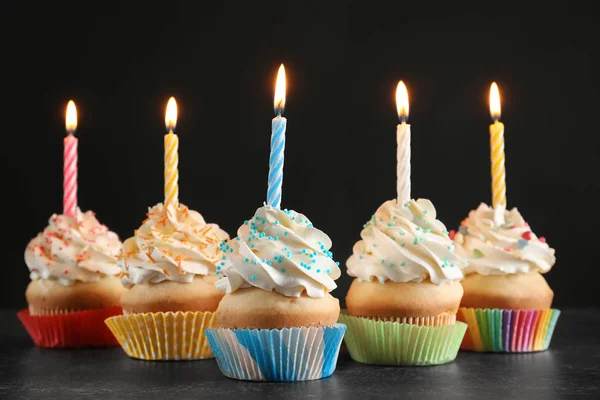 Magdalenas de cumpleaños con velas en la mesa sobre fondo negro —  Fotos de Stock