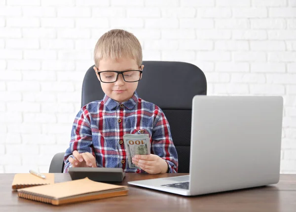 Cute little boy counting money at table indoors