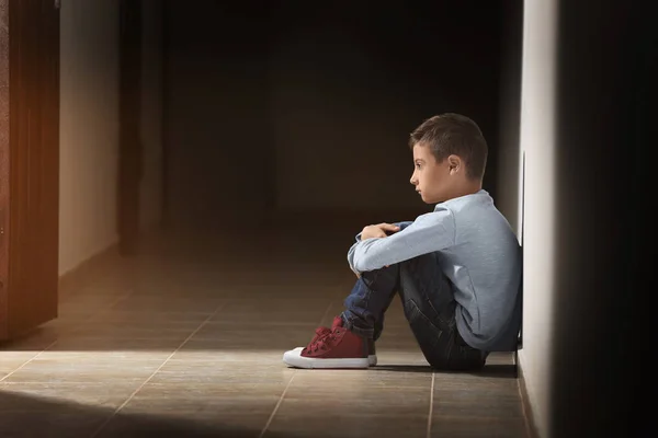 Расстроенный маленький мальчик сидит в коридоре — стоковое фото