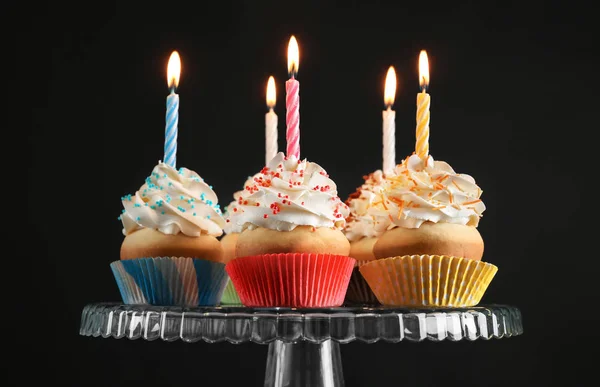 Birthday cupcakes with candles on dessert stand against black background