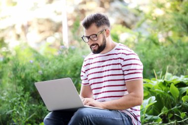 Genç blogger parkta dizüstü bilgisayar kullanarak