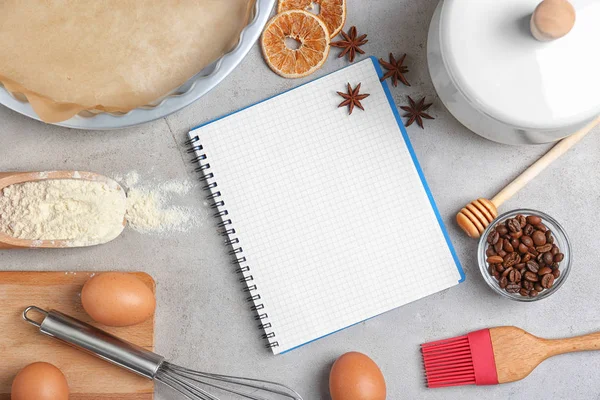 Kitchen utensils with ingredients for pastries and notebook on light background