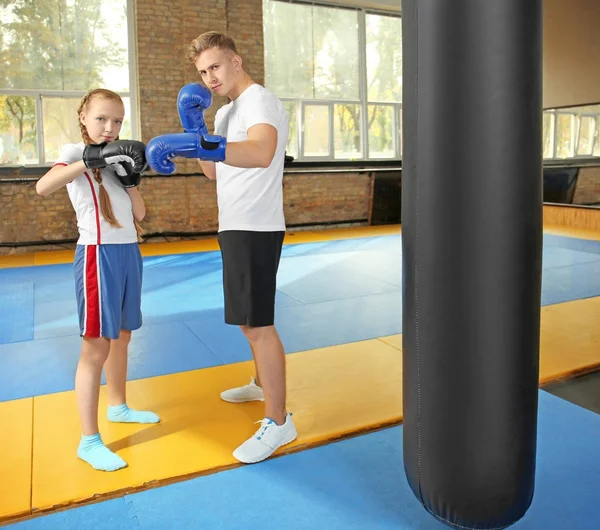 Little girl with trainer in boxing gloves indoors