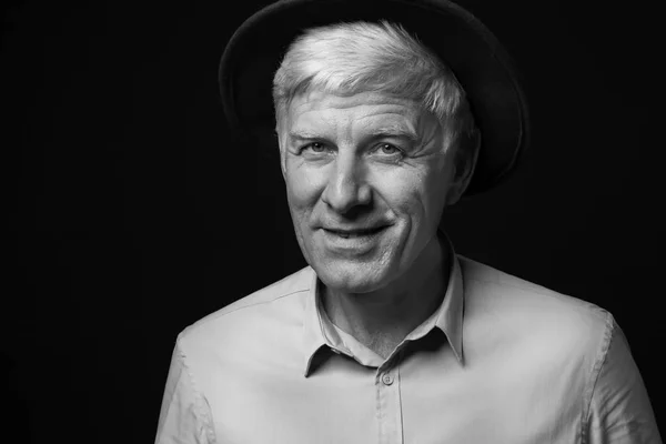 Портрет усміхненого зрілого чоловіка з капелюхом на темному тлі — стокове фото