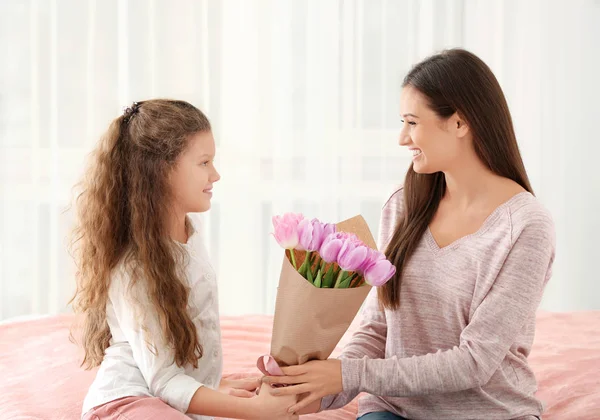 Söt liten flicka ger Tulpanbukett till hennes mamma inomhus. Mors dag firande — Stockfoto