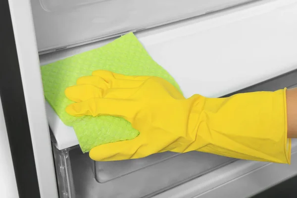 Woman cleaning refrigerator with rag, closeup