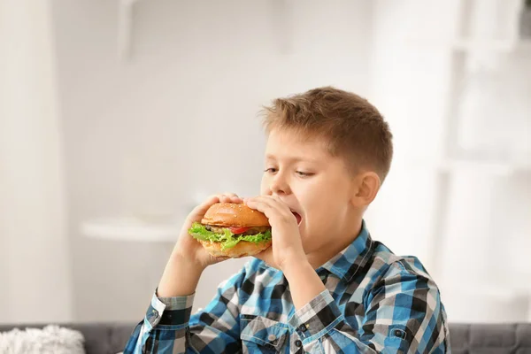 Overweight boy eating burger at home