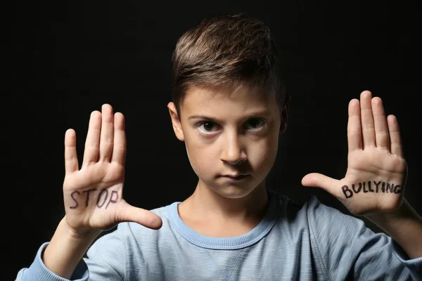 Маленький хлопчик зі словами "Стоп знущання" на руках на чорному тлі — стокове фото