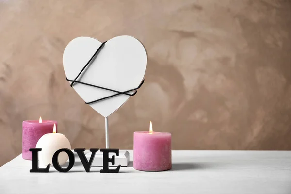 Word LOVE, decorative heart and candles on table