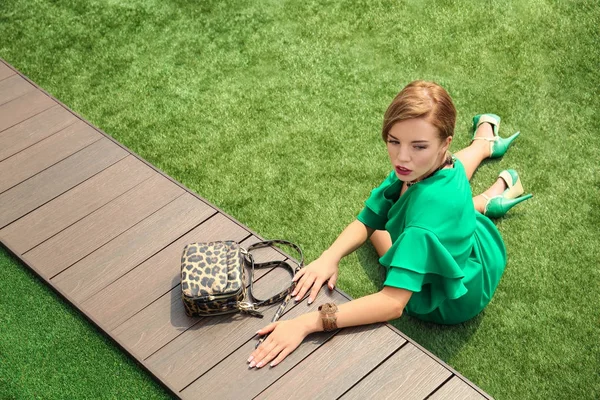 屋外の新鮮な草の上に座って緑のドレスを着た美しい女性 — ストック写真
