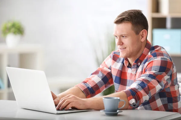 Jeune homme utilisant un ordinateur portable à la table à l'intérieur — Photo