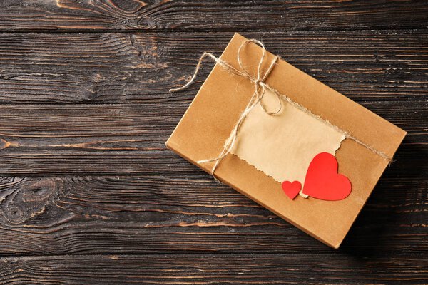 Gift box with card and paper hearts on wooden background