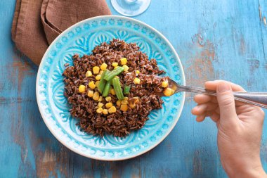 Çatal kırmızı pirinç ve Mısır ile plaka üzerinde tutan el