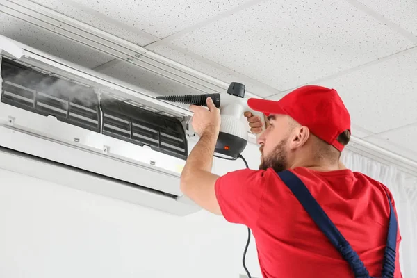 Mannelijke technicus schoonmaken van airconditioner binnen — Stockfoto