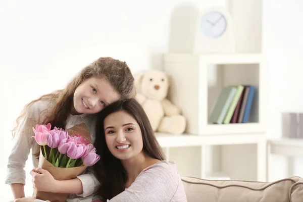 Giovane donna e sua figlia con bouquet di tulipani in casa. Festa della mamma celebrazione — Foto Stock