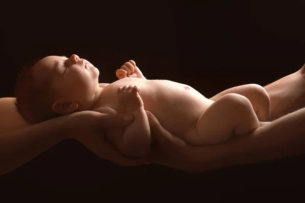 Руки родителей, держащих маленького милого ребенка на темном фоне — стоковое фото
