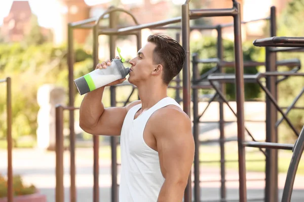 Handsome young man with protein drink in shaker outdoors