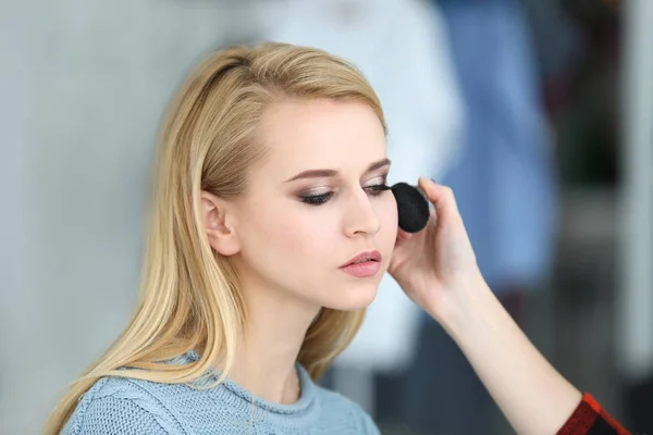 Professionelle Künstlerin schafft Make-up für schönes Modell auf verschwommenem Hintergrund — Stockfoto