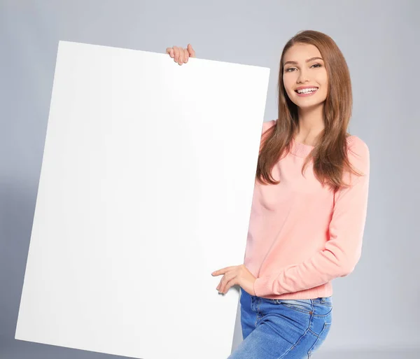 灰色の背景の空白の広告ボードを持つ若い女性 — ストック写真