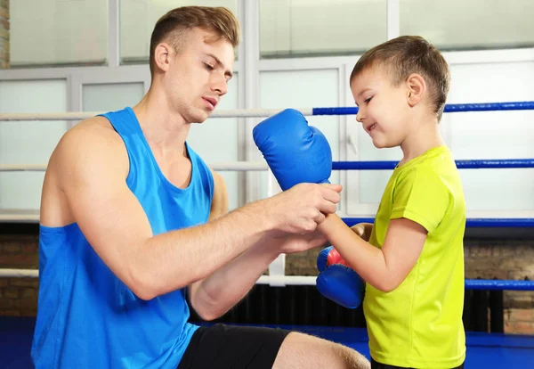 Entrenador ayudando a niño pequeño a ponerse guantes de boxeo en el gimnasio — Foto de Stock