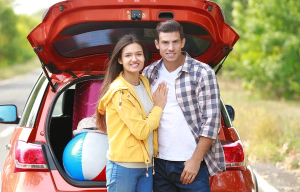 Happy couple with luggage near car