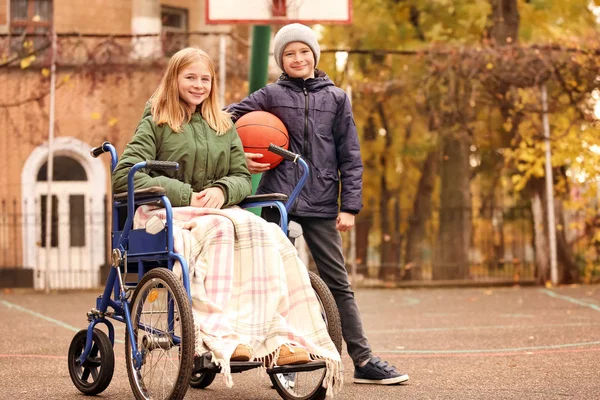 Niña en silla de ruedas y su hermano con pelota en el patio —  Fotos de Stock