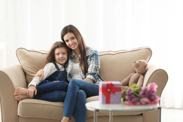 Молодая мать и ее дочь обнимаются на диване в помещении — стоковое фото