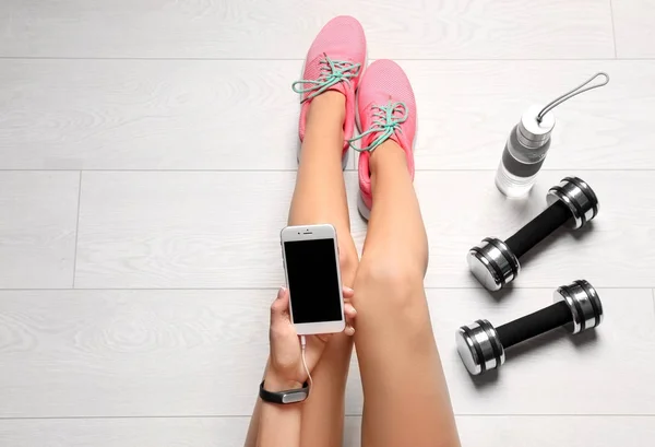 年轻女子用手机坐在靠近哑铃的地板上 平躺着 准备健身房锻炼 — 图库照片
