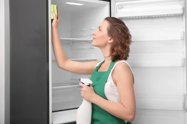 Beautiful woman cleaning empty refrigerator in kitchen