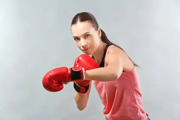 Strong woman in boxing gloves on grey background