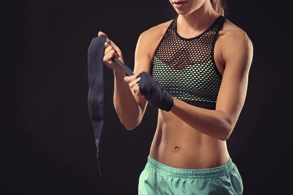 Boxer woman applying wrist wraps on black background